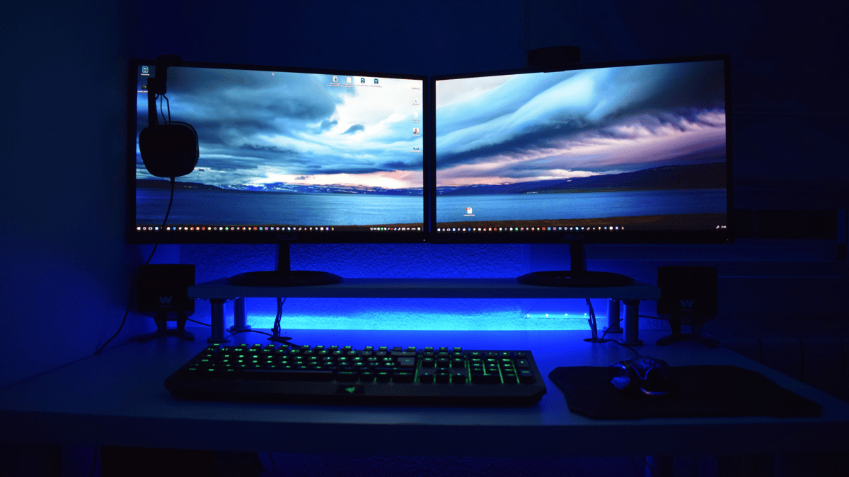 Et skrivebord med to skjermer, et tastatur, en mus og et headset